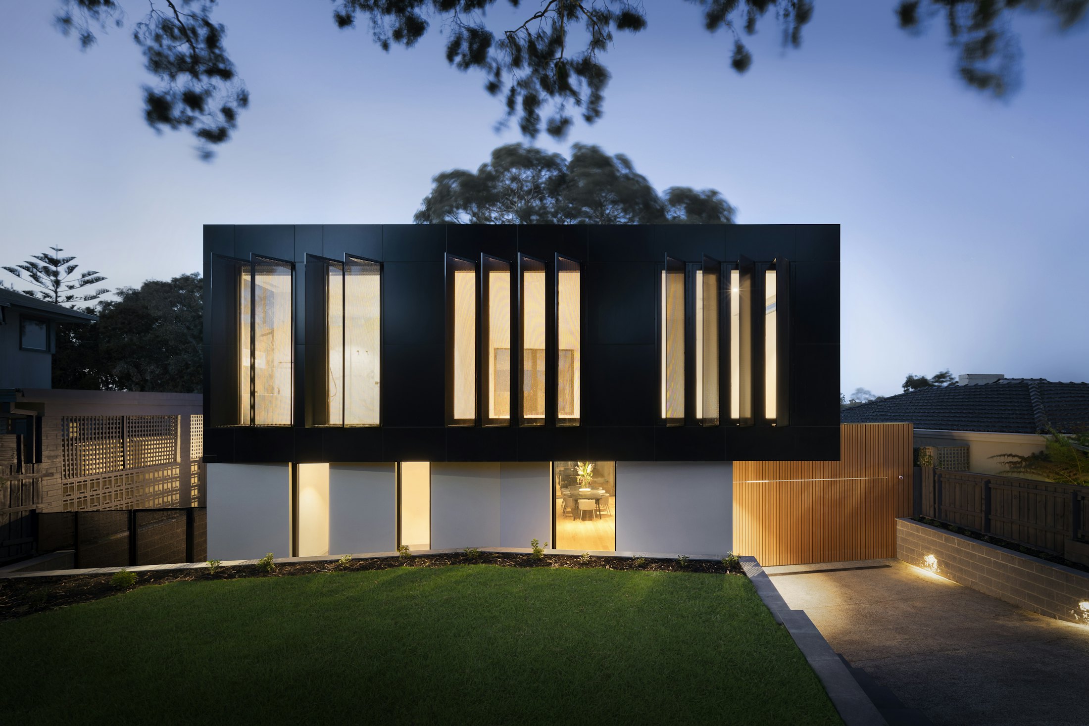 A modern two-storey home with a large glazed rear extension, lit at dusk